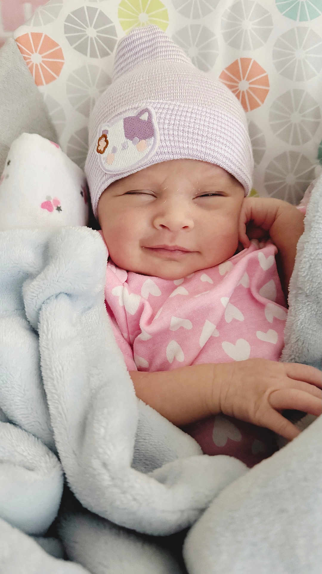 Norrakkesa is registered to the contest to win money with this photo: baby, blanket, hat, pink_clothing, heart_pattern, smiling, sleepy, cute, infant, soft_texture, cozy, child, face, headwear, newborn, wrapped, resting, indoors, cute_expression, warm