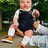 baby, child, person, smile, overalls, socks, shoes, hand, outdoor, park, trees, greenery, cute, portrait, infant, happy, holding, casual_clothing, nature, daylight