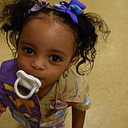 Araya joined the competition — help win amazing prizes! toddler, child, pacifier, hair_bow, curly_hair, colorful_clothing, paint_splatter, floor, indoor, portrait, young_child, cute, looking_up, big_eyes, earrings, necklace, playful, expression, person, closeup