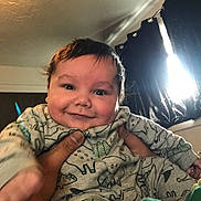 Eric joined the competition — help win amazing prizes! baby, smile, child, onesie, dinosaur_pattern, hands, indoor, curtains, light, ceiling, person, face, clothing, happy, cute, young_child, infant, portrait, holding, cozy