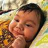Eric is registered to the contest to win money with this photo: baby, child, infant, smiling, face, hand, toy, pillow, patterned, clothing, indoor, closeup, cute, young, person, portrait, soft_light, happy, resting, cozy