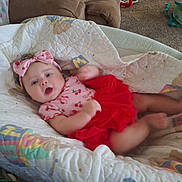 Lilith joined the competition — help win amazing prizes! baby, child, infant, portrait, lying_down, smiling, wide_eyed, bow, red_dress, floral_clothing, playpen, blanket, cushion, indoors, living_room, couch, carpet, toys, home, photography