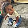 Sekani is registered to the contest to win money with this photo: toddler, child, indoor, carpet, curly_hair, blue_pants, cream_shirt, socks, toy, sitting, person, cute, baby, floor, expression, small_hands, eyes, portrait, casual, home