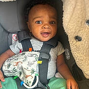 Sekani joined the competition — help win amazing prizes! baby, child, car_seat, safety_harness, toy, animal_print, giraffe, elephant, smile, happy, infant, green_pants, gray_shirt, seat_belt, cute, portrait, indoor, close_up, hand, face