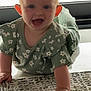 baby, carpet, child, crawling, cute, face, floral_pattern, green_clothing, hand, happy, home, indoor, infant, natural_light, person, playful, smiling, texture, window, young_child