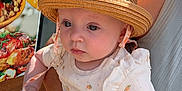 Lou a rejoint le concours — aidez-le/la à gagner de superbes lots ! adult_hand, baby, child, closeup, curious_expression, food_poster, glass_door, hat, holding, infant, light_clothing, outdoor, patterned_clothing, person, portrait, red_nail_polish, straw_hat, sunlight, table, tattoo