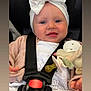 baby, child, car_seat, headband, bow, pacifier, stuffed_toy, pink_sweater, white_clothing, smile, face, hands, seatbelt, closeup, indoor, infant, cute, happy, portrait, baby_accessories