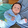 Yaman is registered to the contest to win money with this photo: baby, infant, striped_clothing, person, adult, holding, indoor, wooden_floor, table, papers, home, comfort, relaxed, seated, casual, light, face, hand, pajamas, striped_shirt