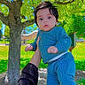 baby, child, person, outdoor, park, tree, grass, sunlight, hand, clothing, blue_pajamas, face, playing, nature, daylight, greenery, holding, cute, young_child, expression