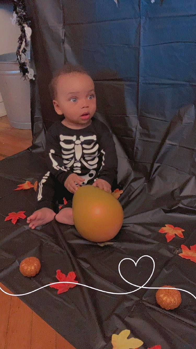 Chase is registered to the contest to win money with this photo: baby, calabaza, child, comfort, floor, flooring, fun, hardwood, living_room, orange, person, plant, play, pumpkin, room, sitting, surprise, toddler, toy, tree