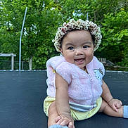 Livia joined the competition — help win amazing prizes! baby, child, smile, flower_crown, pink_vest, outdoor, trampoline, greenery, trees, happy, sitting, cute, infant, nature, playful, portrait, young_child, sunlight, casual_clothing, fun