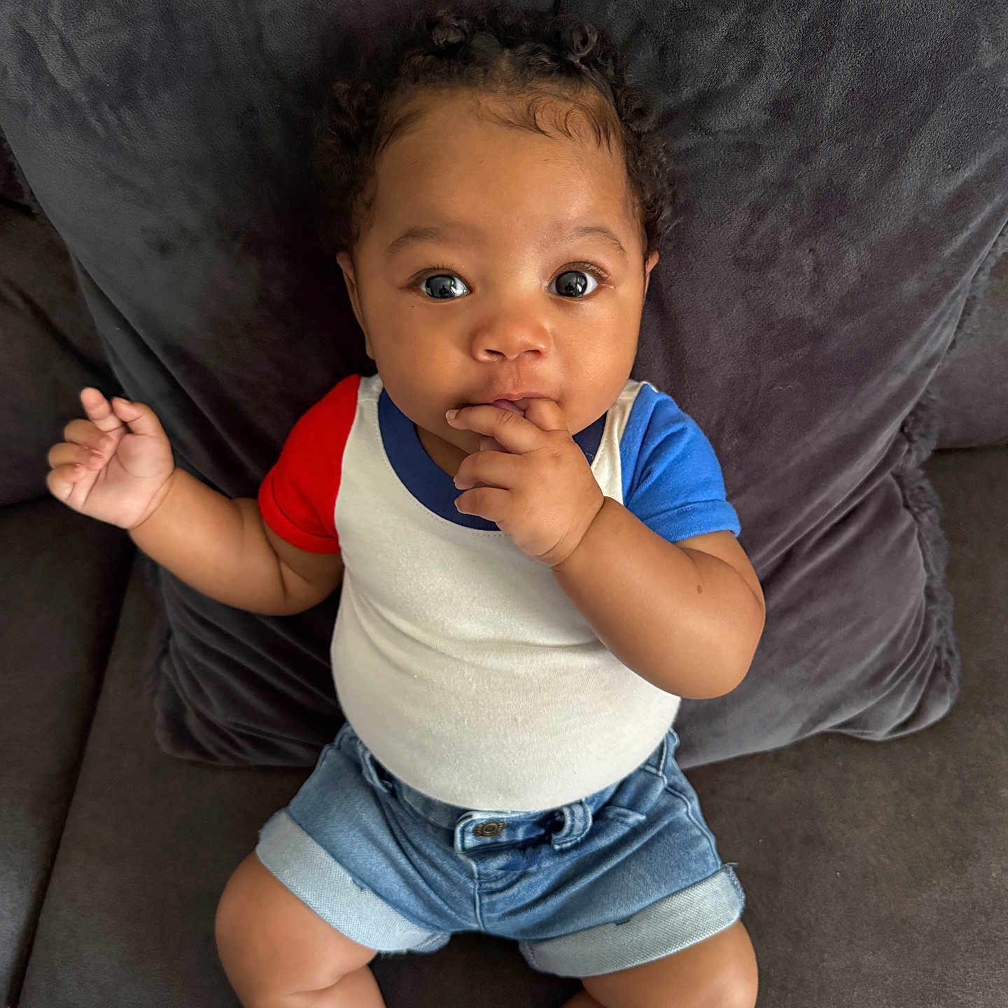 Millionna is registered to the contest to win money with this photo: baby, child, clothing, comfortable, couch, curly_hair, cute, denim_shorts, eyes, face, fingers, hand, home, indoor, infant, plush, portrait, sitting, sock, tshirt
