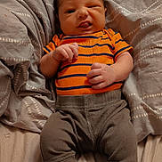 Wynston is registered to the contest to win money with this photo: baby, infant, striped_shirt, orange_shirt, gray_pants, blanket, patterned_blanket, lying_down, cheeky_expression, tongue_out, one_eye_closed, indoors, bedroom, fabric, comfort, cute, small_hands, newborn, young_child, person