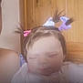 baby_doll, blurred, caucasian_skin, child, child_like, closed_eyes, doll_clothing, face, hair_bows, indoor, person, pigtails, pink_bow, portrait, purple_bow, soft_toy, stuffed_toy, toy, white_bow, wooden_background