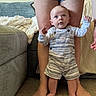 Lincoln is registered to the contest to win money with this photo: adult, baby, blanket, carpet, casual_clothing, child, couch, cozy, curious, feet, home, indoor, legs, looking_up, overalls, person, portrait, standing, striped_clothing, supporting
