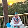 Lincoln joined the competition — help win amazing prizes! baby, high_chair, crown, balloon, sunset, outdoor, deck, wooden_railing, greenery, smiling, happy, celebration, blue, white, polka_dot, infant, child, party, nature, portrait
