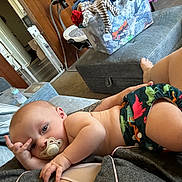 Lincoln is registered to the contest to win money with this photo: baby, bottle, casual, clothes, comfort, couch, diaper, dinosaur_pattern, foot, hand, home, indoor, infant, laundry_basket, living_room, pacifier, person, relaxing, skin, tattoo