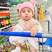 Eimmy joined the competition — help win amazing prizes! baby, child, shopping_cart, grocery_store, pink_hat, pom_poms, blanket, socks, curious, shelf, beverages, soda, shopping, retail, infant, cute, indoor, clothing, person, cart_handle