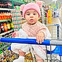 baby, child, shopping_cart, grocery_store, pink_hat, pom_poms, blanket, socks, curious, shelf, beverages, soda, shopping, retail, infant, cute, indoor, clothing, person, cart_handle