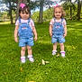 toddler, child, outdoor, grass, trees, summer, sunny, denim_overalls, pink_bow, shoes, greenery, park, nature, cute, two_children, standing, daylight, casual_clothing, happy, playful