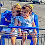toddler, child, shopping_cart, blue_dress, yellow_bow, parking_lot, car, summer, outdoor, cute, twins, sitting, footwear, sunlight, curious, playful, person, daytime, vehicle, plastic_seat