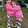 child, toddler, hug, outdoor, grass, tree, pink_hoodie, plaid_pants, smile, happy, cute, person, sibling, friendship, nature, playing, shoes, vehicle, daylight, affection