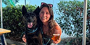 Jack joined the competition — help win amazing prizes! beer, bench, black_dog, canopy, casual, daylight, dog, glass, greenery, happy, leash, nature, outdoor, pet, picnic_table, portrait, smiling, string_lights, sunglasses, woman