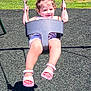 casual_clothing, chains, child, daylight, fence, fun, grass, happy, outdoor, park, person, pigtails, playground, recreation, sandals, shadow, smiling, sunny, swing, toddler