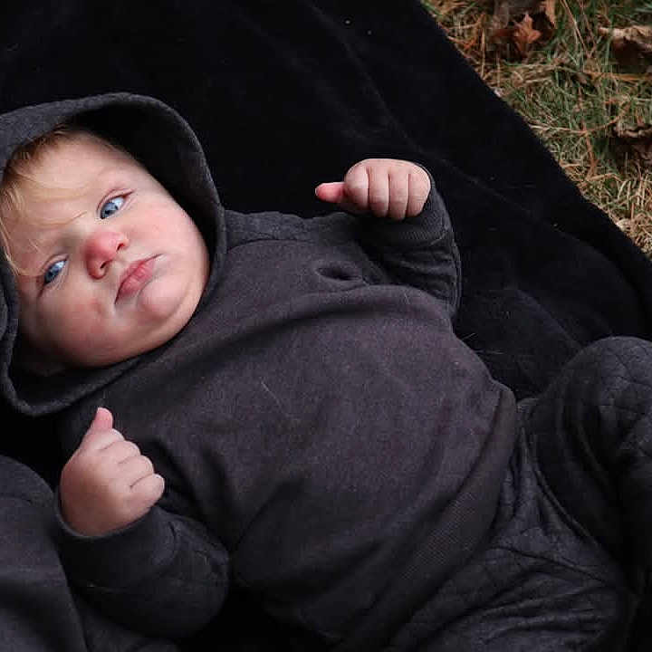 Sullivan is registered to the contest to win money with this photo: baby, blanket, clothing, coat, face, grass, happy, head, hood, hoodie, jacket, knitwear, person, photography, plant, portrait, smile, sweater, sweatshirt, t_shirt