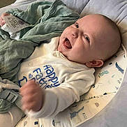 Roman is registered to the contest to win money with this photo: baby, infant, smiling, laughing, clothing, onesie, blanket, baby_seat, dinosaur_print, happy, face, head, hand, cozy, indoors, person, cute, child, seat_belt, comfort