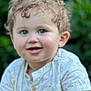 baby, blue_eyes, child, curly_hair, cute, face, greenery, happy, head, light_clothing, nature, outdoor, person, portrait, shirt, skin, smiling, toddler, young, young_child