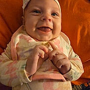 Cecilia is registered to the contest to win money with this photo: baby, bib, chubby_cheeks, close_up, cozy, cute, fingers, flower_pattern, hands, happy, headband, indoor, infant, onesie, orange_background, pillow, portrait, sleepwear, smiling, tongue_out