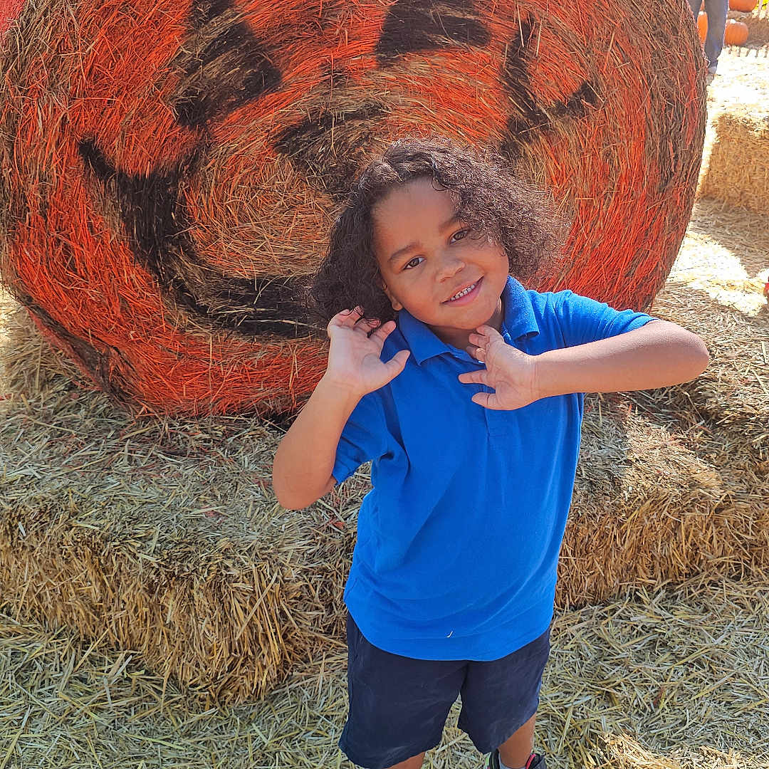 Rayden joined the competition — help win amazing prizes! autumn, blue_shirt, boy, casual_clothing, child, curly_hair, decoration, fall_festival, festival, fun, hay_bale, jack_o_lantern, neon_sneakers, outdoor, playful, posing, pumpkin_face, smiling, straw, sunny_day