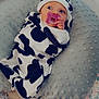 baby, infant, pacifier, cow_print, hat, pillow, blanket, floral_bedding, soft_texture, lying_down, clothing, cute, child, indoors, bed, newborn, comfort, rest, person, sleepwear