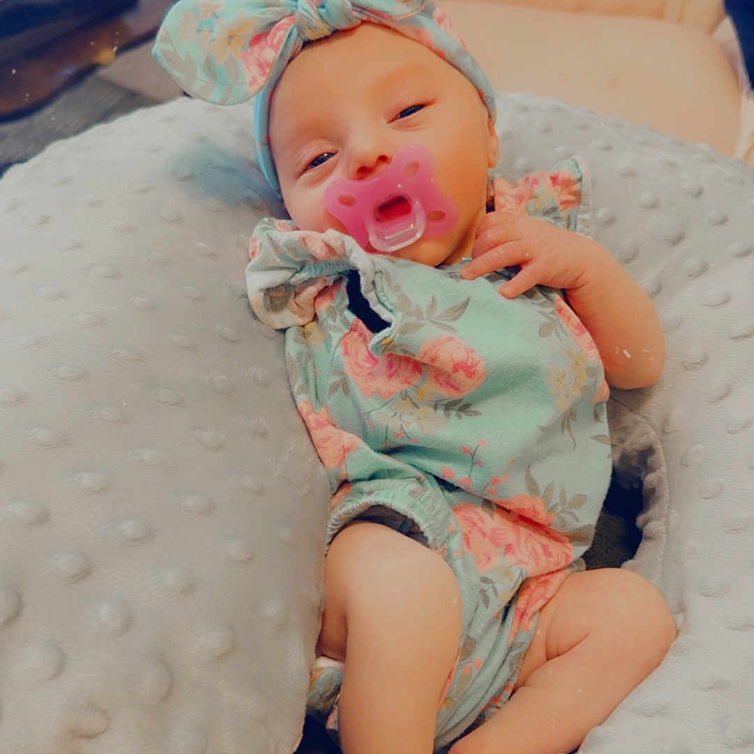 Carolynn is registered to the contest to win money with this photo: adorable, baby, child, comfort, cushion, cute, feet, floral_outfit, gray, hand, headband, indoors, infant, legs, newborn, pacifier, person, resting, sleepy, soft_texture
