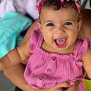 Daniella is registered to the contest to win money with this photo: baby, child, smiling, pink_outfit, headband, happy, person, cute, portrait, infant, hands, holding, curly_hair, earrings, buttoned_clothing, indoor, skin, fashion, closeup, expressive