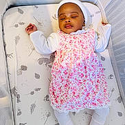 Amelia is registered to the contest to win money with this photo: baby, sleeping, crib, mattress, floral_dress, white_tights, headwear, infant, peaceful, child, bedtime, cute, pattern, animal_print, leaf_print, soft_lighting, indoors, portrait, resting, small_hands