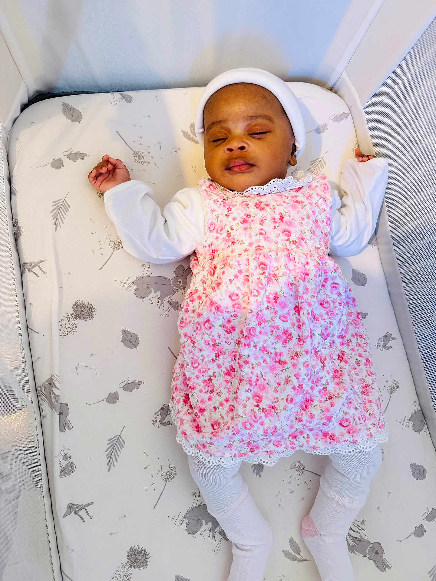 Amelia is registered to the contest to win money with this photo: baby, sleeping, crib, mattress, floral_dress, white_tights, headwear, infant, peaceful, child, bedtime, cute, pattern, animal_print, leaf_print, soft_lighting, indoors, portrait, resting, small_hands