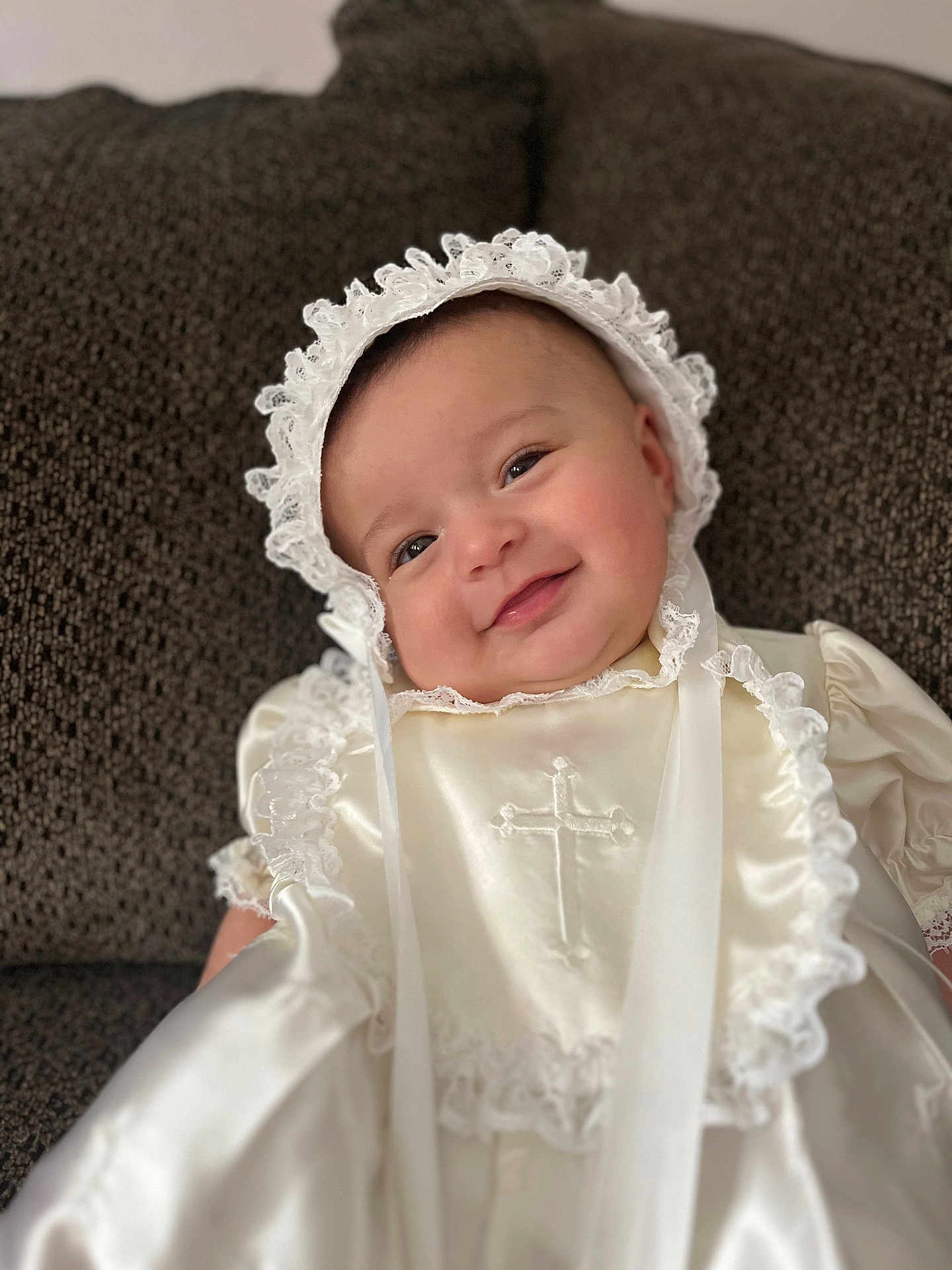 Lilia joined the competition — help win amazing prizes! baby, infant, child, smiling, bonnet, lace, christening_gown, cross, white_clothing, satin, portrait, close_up, rosy_cheeks, couch, soft_texture, happy, cute, indoors, celebration, religious