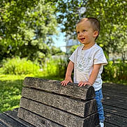 Lyzio a rejoint le concours — aidez-le/la à gagner de superbes lots ! toddler, child, bench, outdoor, greenery, sunlight, white_tshirt, blue_jeans, happy, smiling, nature, wood, park, daylight, portrait, person, casual_clothing, expression, curious, standing