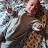 baby, infant, striped_clothing, blanket, bear_pattern, face, hand, lying_down, cute, child, onesie, soft_fabric, cozy, portrait, indoors, young_child, small_hands, bedtime, comfort, sleepwear