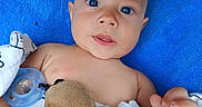 Atlas is registered to the contest to win money with this photo: baby, infant, blue_cushion, blanket, plush_toy, pacifier, child, cute, portrait, indoors, soft_toy, lying_down, hand, face, expression, skin, head, eyes, young, cozy