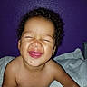 baby, infant, child, portrait, smiling, happy, eyes_closed, curly_hair, face, bare_shoulders, bed, bedding, pillow, bedroom, purple_wall, indoors, close_up, sitting, joyful, photography