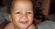 Willow is registered to the contest to win money with this photo: baby, child, smiling, portrait, curly_hair, face, eyes, nose, mouth, drool, bare_shoulders, bedroom, bed, blanket, home, indoors, toy, cozy, close_up, photograph