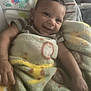 Sylas is registered to the contest to win money with this photo: baby, smiling, blanket, child, infant, cushion, seat, face, arm, happy, indoor, toddler, cozy, cute, plush, striped_clothing, comfort, colorful, animal_print, portrait