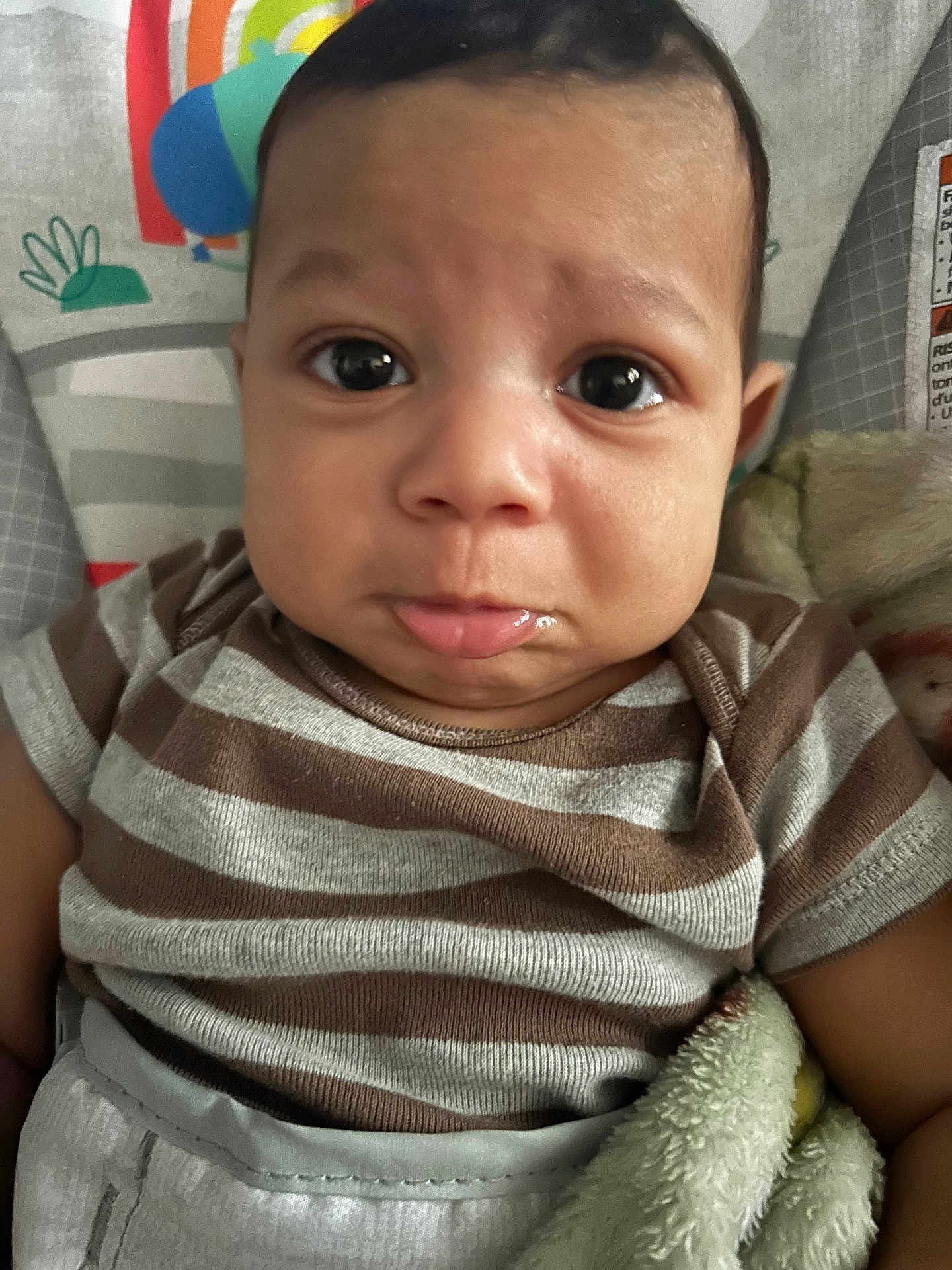 Sylas is registered to the contest to win money with this photo: baby, child, face, expression, eyes, pout, clothing, striped_shirt, blanket, infant, seat, colorful, soft_texture, portrait, indoors, cute, person, young_child, closeup, comfort