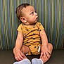 Sylas is registered to the contest to win money with this photo: baby, infant, child, onesie, socks, striped_couch, curious, sitting, indoor, furniture, young_child, portrait, looking_away, clothing, cute, skin, head, hand, footwear, patterned