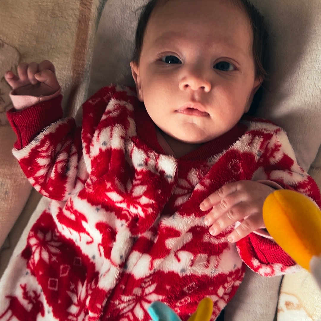 Talya participe au concours pour gagner de l'argent avec cette photo : baby, bed, blanket, child, curious, cute, face, hand, holiday, indoors, infant, lying_down, newborn, onesie, portrait, red_clothing, soft_toy, toy, warm, white_clothing