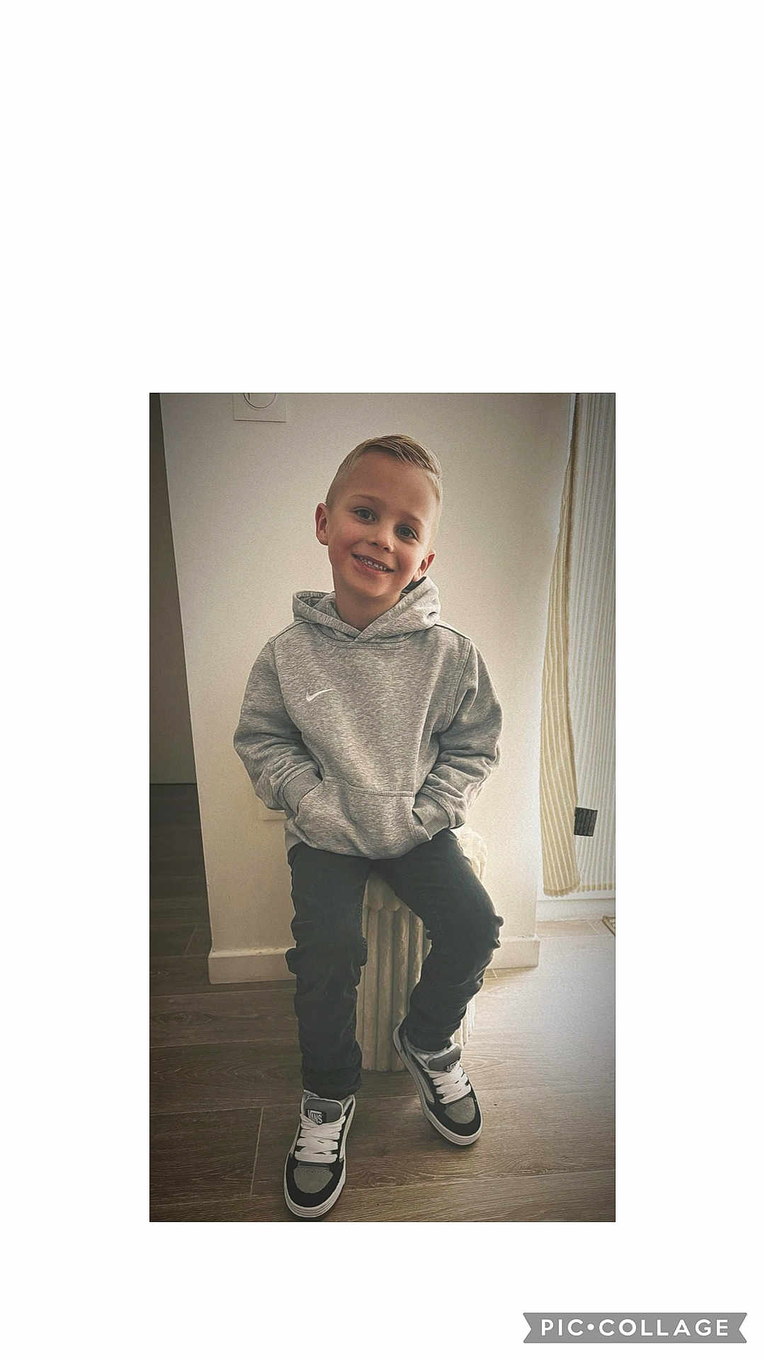 Nael a rejoint le concours — aidez-le/la à gagner de superbes lots ! child, boy, smile, hoodie, grey_hoodie, sneakers, black_pants, indoor, radiator, floor, wooden_floor, casual, portrait, happy, young, person, sitting, hands_in_pockets, light, curtain