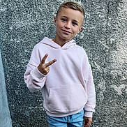 Mathis a rejoint le concours — aidez-le/la à gagner de superbes lots ! child, boy, peace_sign, hoodie, light_pink, blue_jeans, smile, casual_clothing, urban, wall, texture, portrait, standing, young, outdoor, cool, confident, person, fashion, casual